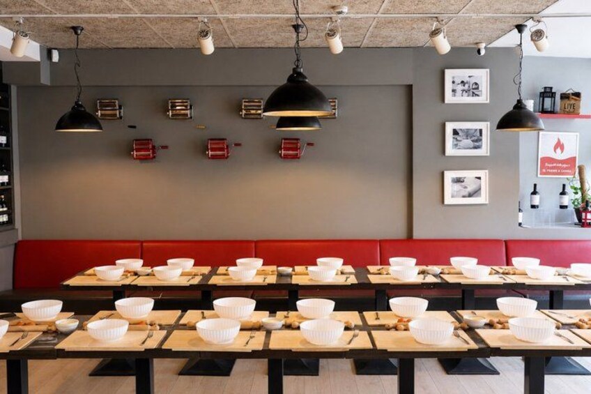 L’intérieur d’un restaurant, avec des tables dressées pour le service, des sièges rembourrés de couleur rouge, des luminaires suspendus et des éléments de décoration fixés aux murs. 2