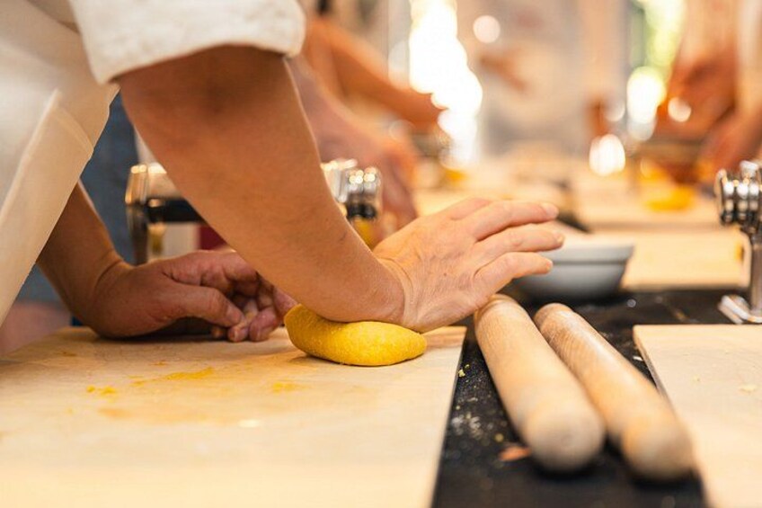 Mani che lavorano la pasta su un piano di lavoro, con mattarelli e una ciotola. 2