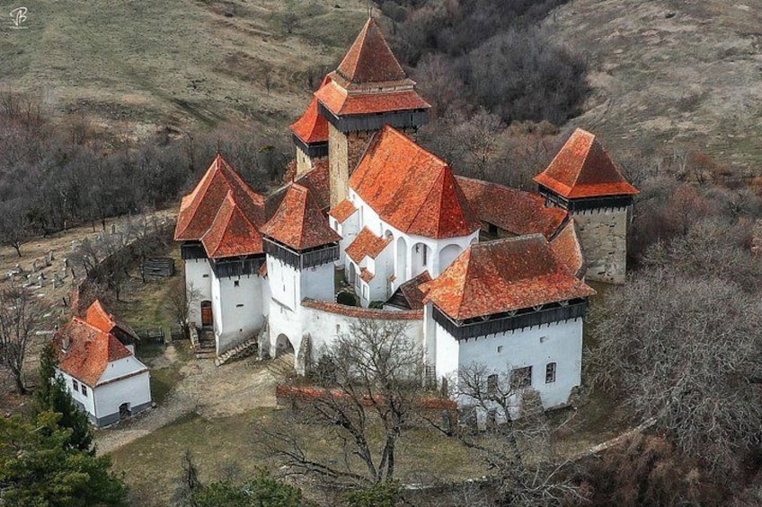 A white building with red roofs and multiple towers, surrounded by a hilly landscape. 4