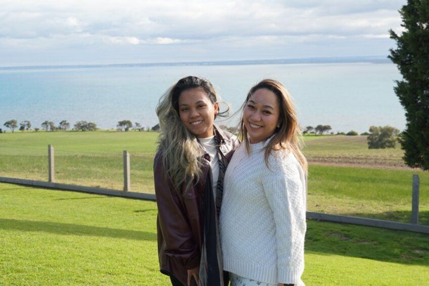 Two people standing on a grassy field with a body of water and trees in the background. 4