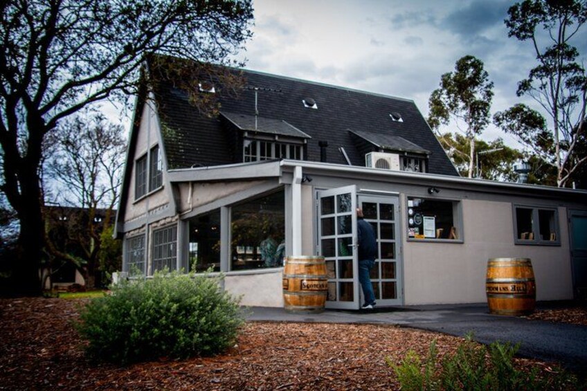 A building with a sloped roof, large windows, and two wooden barrels. 5
