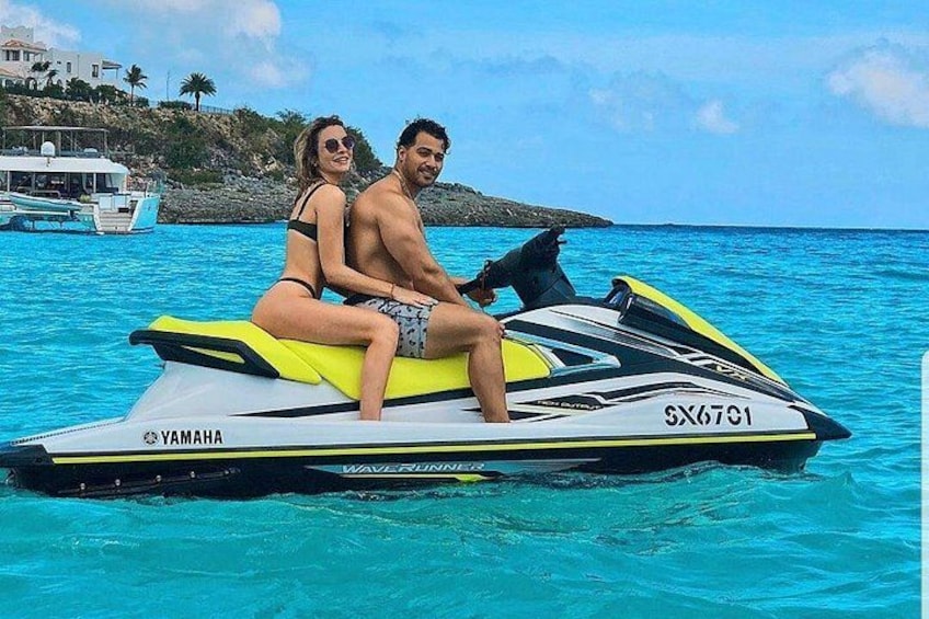Un couple sur un jet ski Yamaha dans des eaux turquoise, avec un bateau et une côte rocheuse en arrière-plan. 4