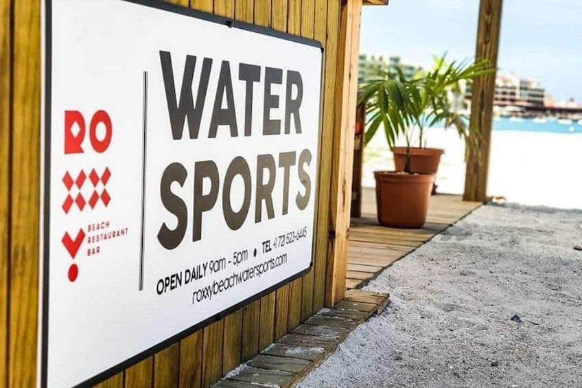 Une enseigne indiquant « Sports nautiques », avec le logo d’un restaurant de plage, une promenade en bois et un pot de fleurs. 2