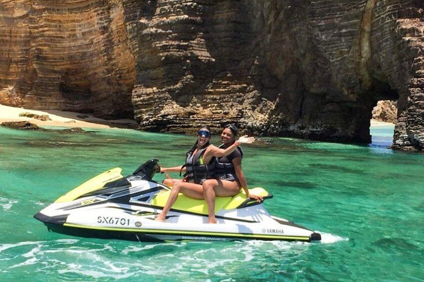 To personer på en jetski i klart vand med klipper i baggrunden. 5