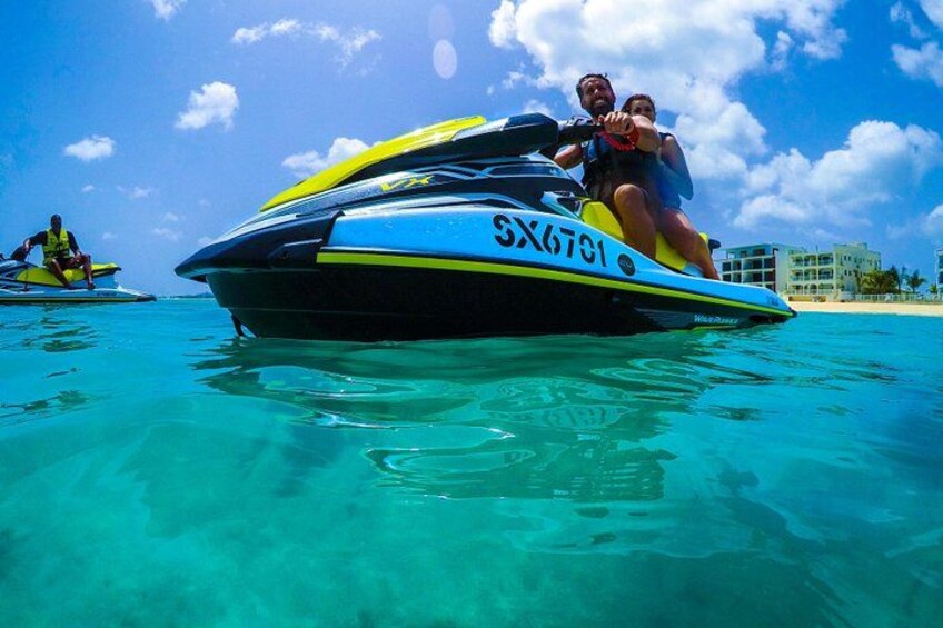 En jetski med nummeret SX6701 på vandet, en anden jetski i baggrunden og en bygning ved kysten. 4