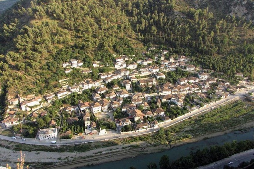 A coastal town with houses along the shoreline, a river, and a forested hill in the background. 1