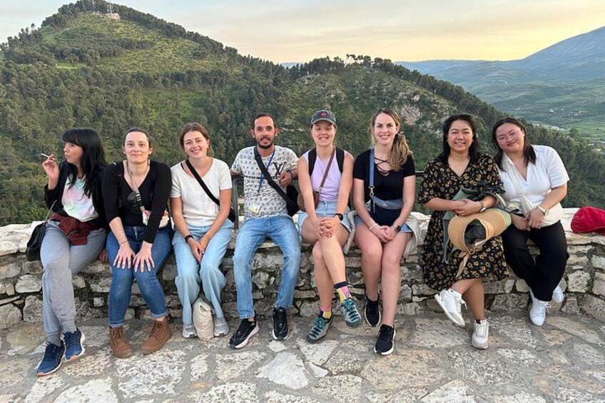 Un grupo de personas sentadas en un muro de piedra con vistas a un paisaje montañoso. 2