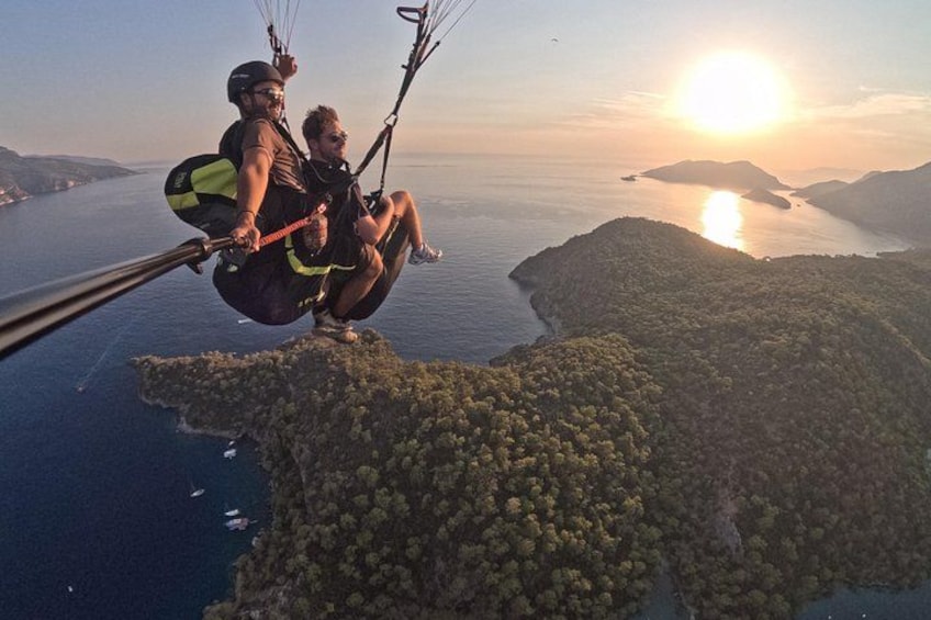 To personer paraglider over et kystlandskab med solnedgang i baggrunden. 4