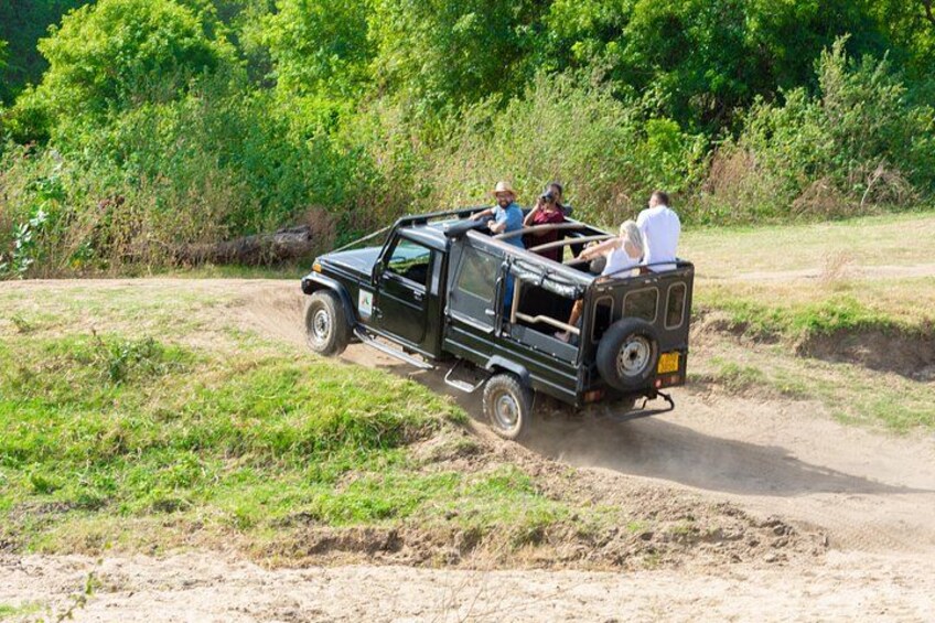 A black off-road vehicle with passengers on a dirt road surrounded by greenery. 1