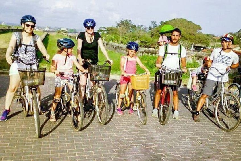 Un grupo de personas en bicicleta, algunas con cestas, sobre un sendero pavimentado con vegetación al fondo. 5