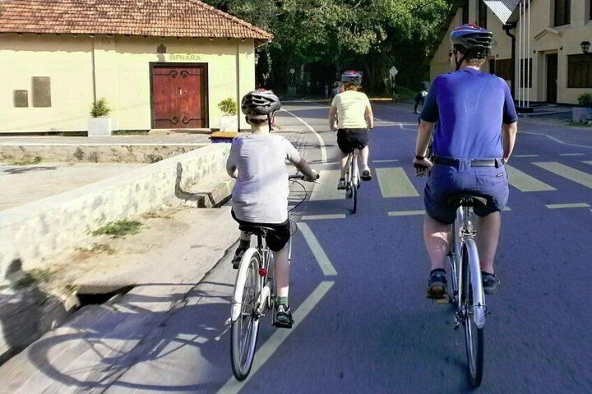 Tres ciclistas pedaleando por una carretera con un edificio que dice 'SIPNARA' al fondo. 3