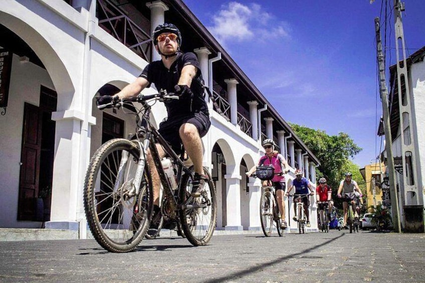Un grupo de ciclistas en una calle adoquinada con edificios blancos y arcos. 4