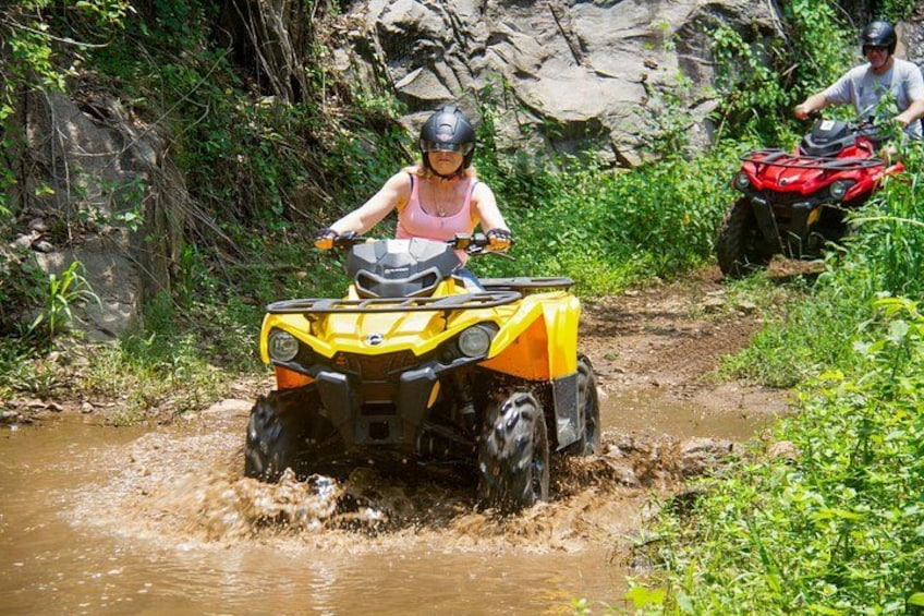 Una persona conduce un cuatrimoto amarillo por un arroyo lodoso. 3