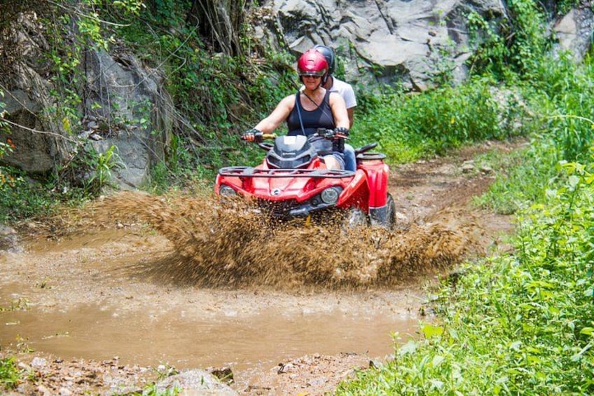 Una persona conduce un cuatrimoto rojo por un arroyo lodoso. 2