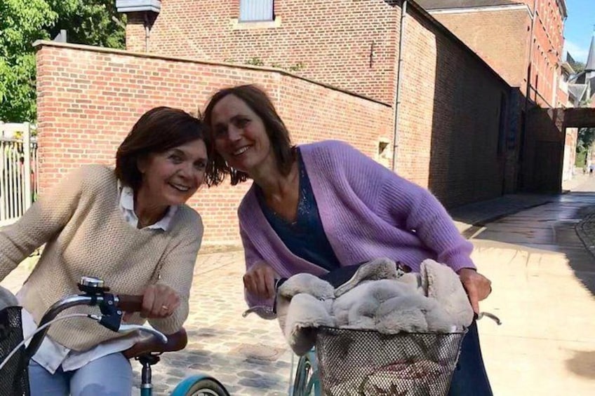 Dos personas en bicicleta, una canasta con un objeto blanco y esponjoso, y un edificio de ladrillo al fondo. 4