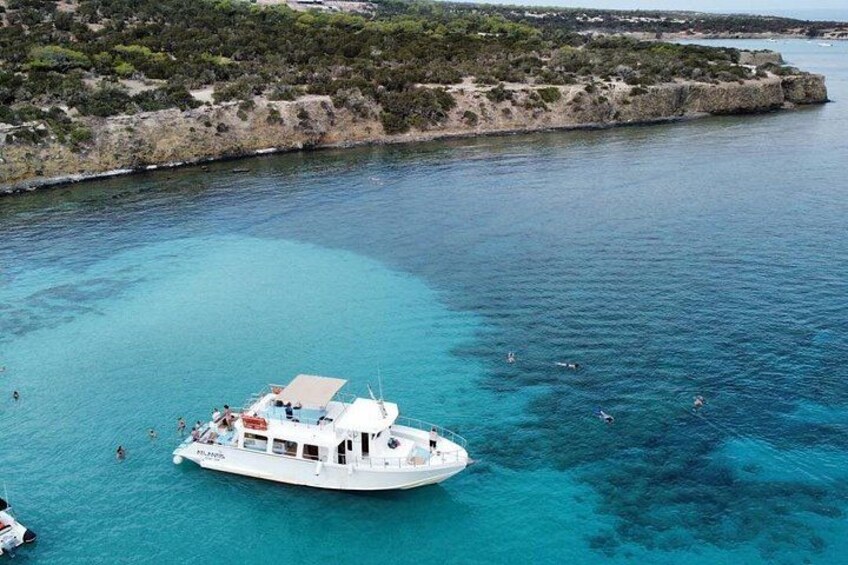 Een witte boot met mensen die in het heldere blauwe water zwemmen nabij een rotsachtige kustlijn. 4