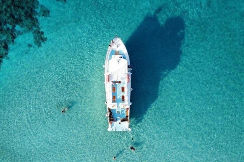 A white boat with a blue and white striped deck anchored in clear turquoise water. 3