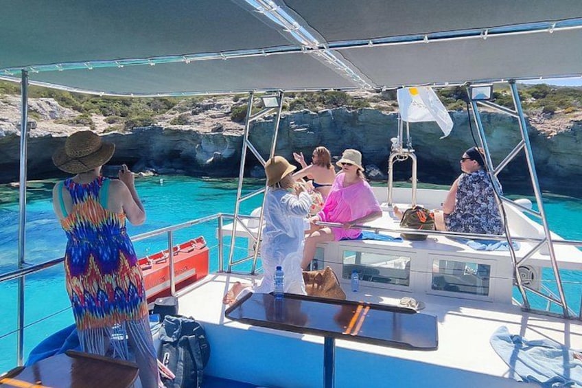 A group of people on a boat with clear blue water and rocky cliffs in the background. 4