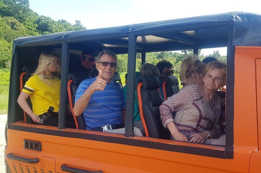 A group of people in an orange vehicle with a roof, likely a safari or tour bus, with a natural landscape in the background. 3