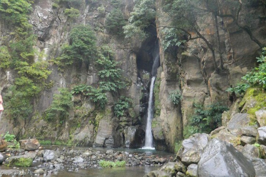A waterfall cascading down a rocky cliff surrounded by lush greenery. 1