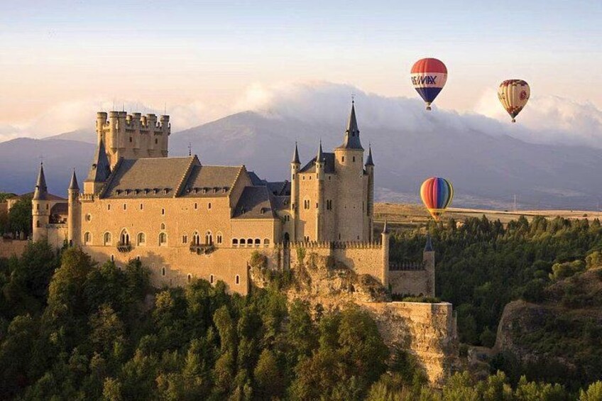 A castle with a moat, surrounded by trees and mountains in the background. 4
