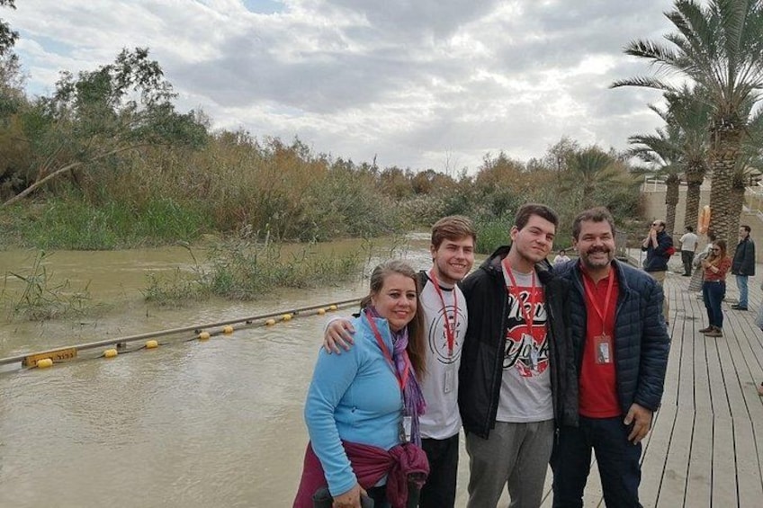 A group of people standing on a wooden boardwalk near a body of water with vegetation in the background. 3