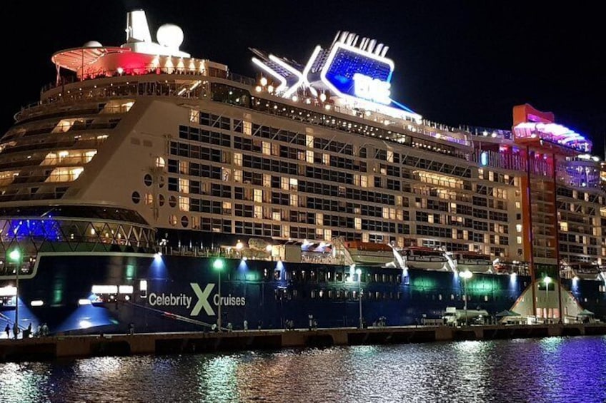 A large cruise ship docked at a port with illuminated signage and multiple decks. 1
