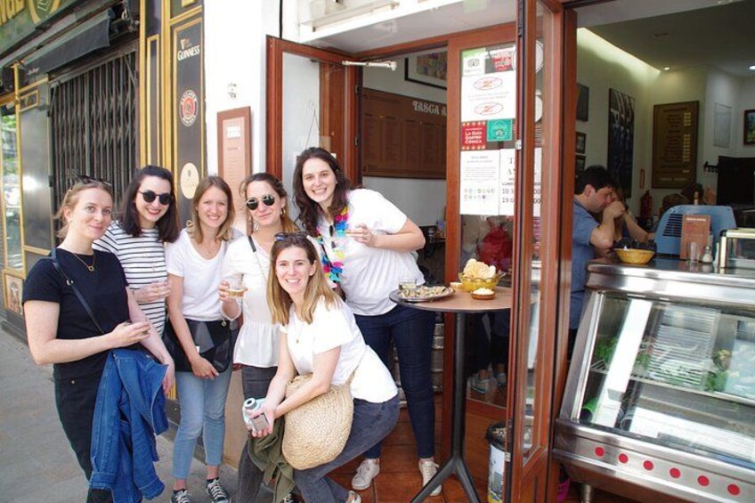 A group of people standing outside a restaurant with a glass display case. 1