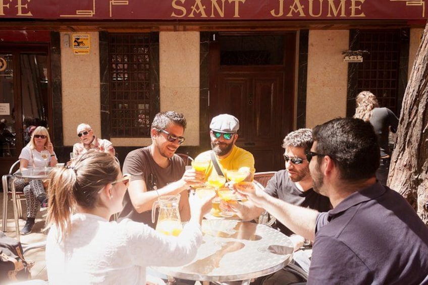 Un grupo de personas brindando con bebidas en una mesa afuera de un edificio con un cartel que dice 'SANT JAUME'. 2
