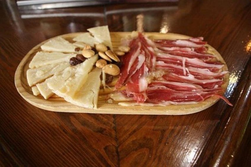 Una tabla de madera con queso en rodajas, embutidos y nueces. 3