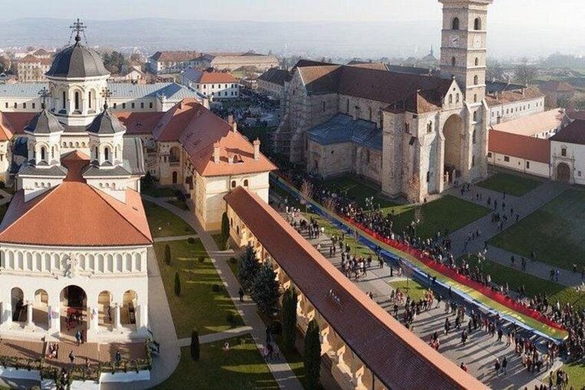 A historic building complex with a prominent tower, a large open plaza, and a long covered walkway. 4