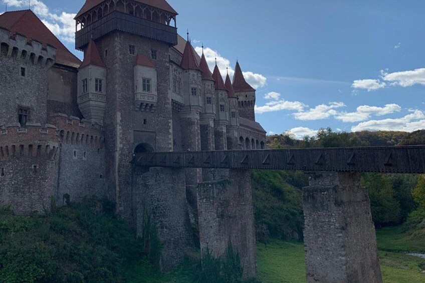 A medieval castle with red-tiled roofs, a stone bridge, and lush greenery. 3