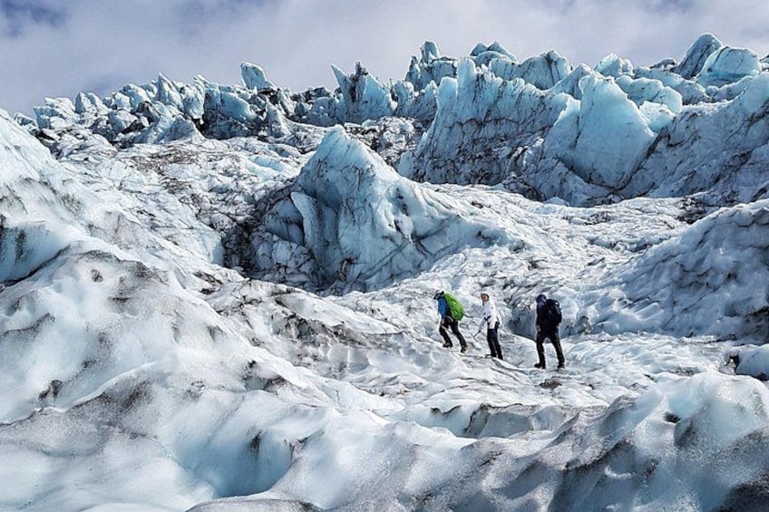 A glacier with ice formations and three hikers. 3