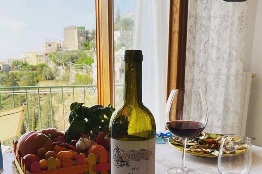 A bottle of wine, a glass of red wine, and a bowl of vegetables on a balcony with a city view. 2