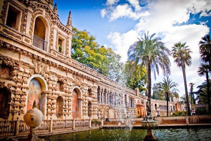 Un edificio histórico con arquitectura detallada, una fuente y palmeras. 2
