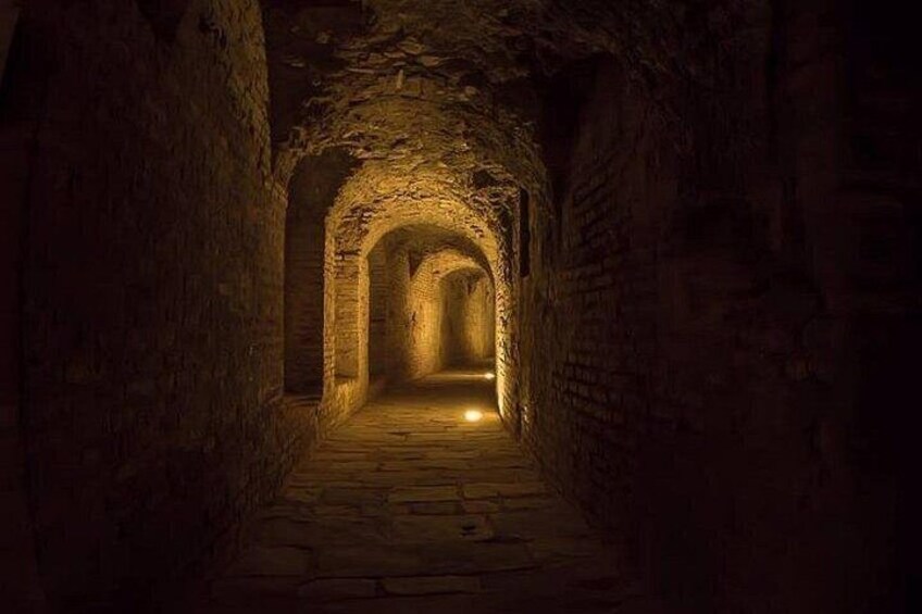 Ein steinerner Tunnel mit gewölbter Decke und einer Lichtquelle am Ende. 1