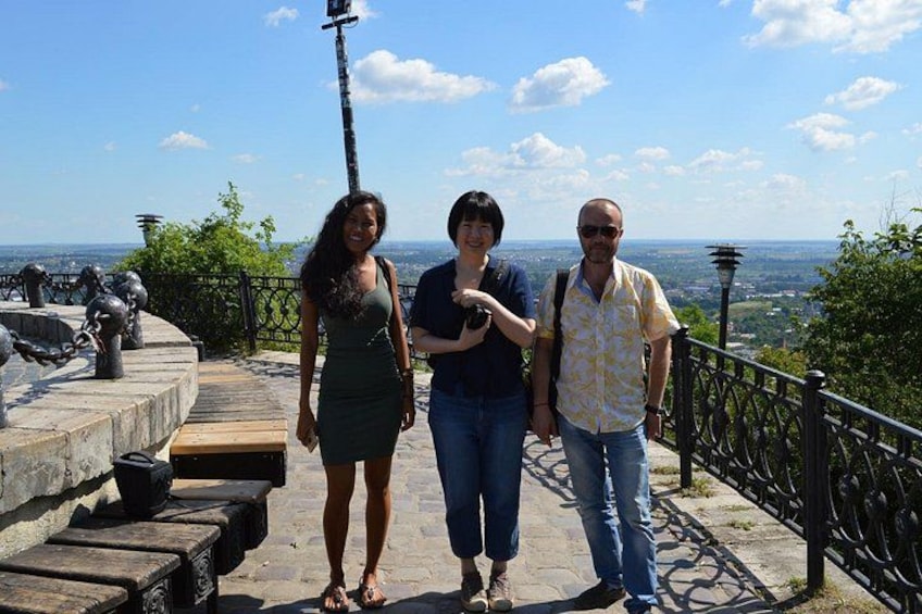 Tres personas caminando por un sendero de piedra con una vista panorámica de una ciudad al fondo. 1