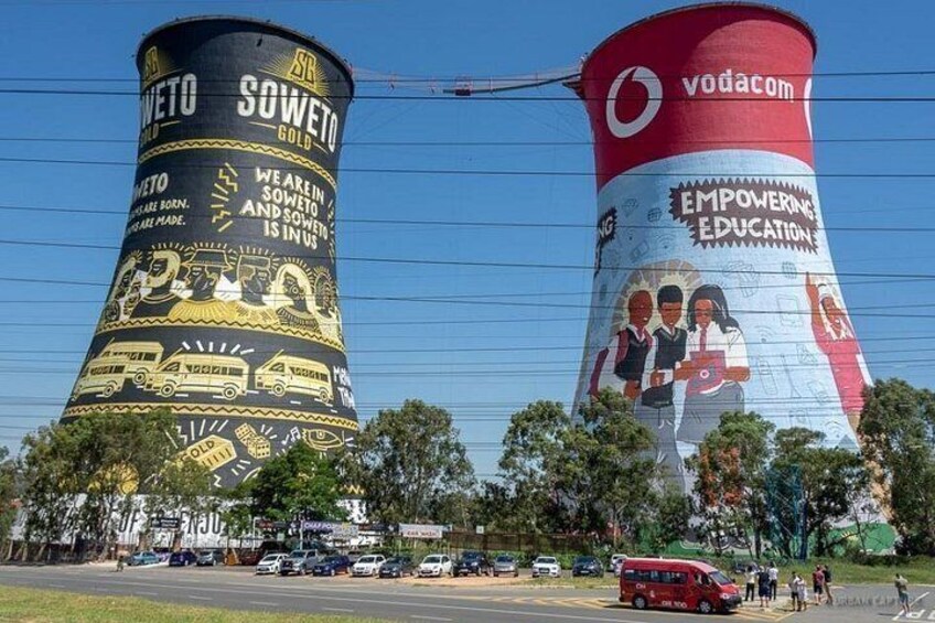 Two large water towers with advertisements, one for SOWETO GOLD and the other for vodacom, with clear skies and a road in the foreground. 5