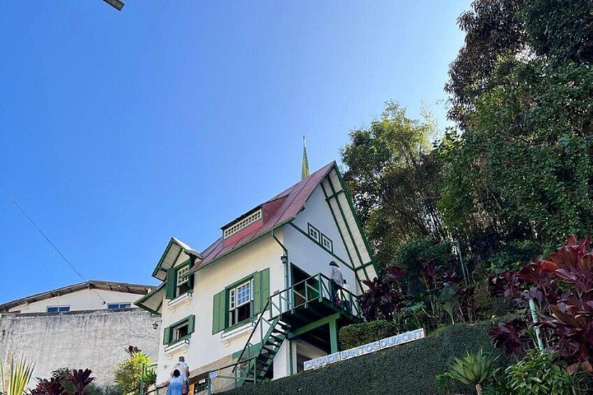 A two-story building with a red roof and green shutters, surrounded by lush greenery. 5