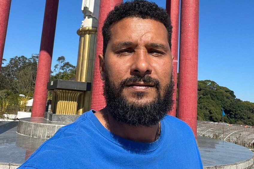A person in a blue shirt standing in front of a structure with red columns and a golden base. 3