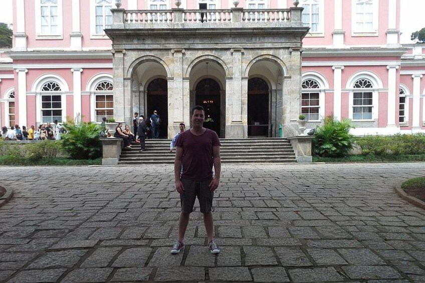 A person standing in front of a pink building with arched doorways and steps leading up to it. 4