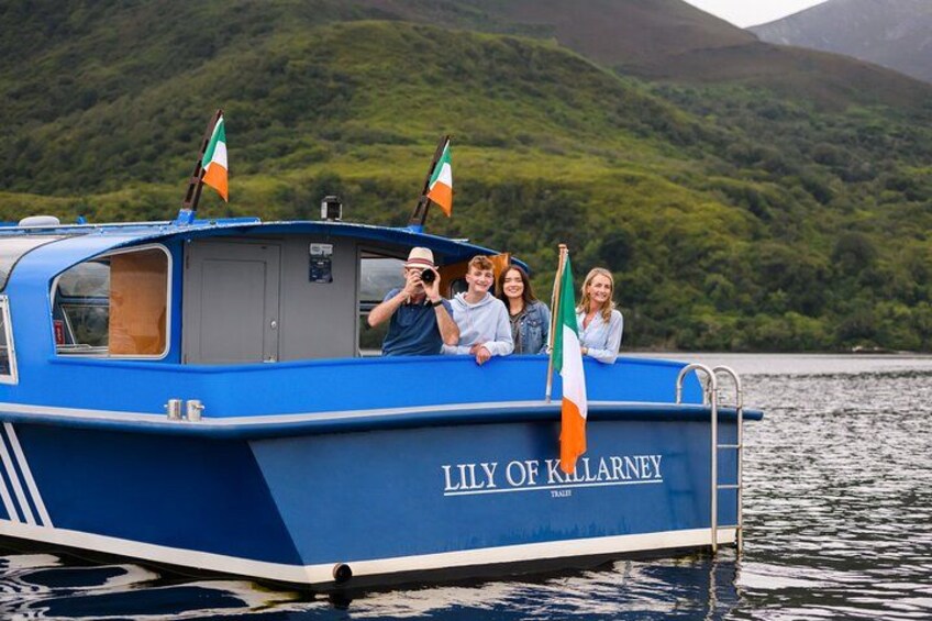A blue boat named "Lily of Killarney" with Irish flags on a lake surrounded by greenery. 4