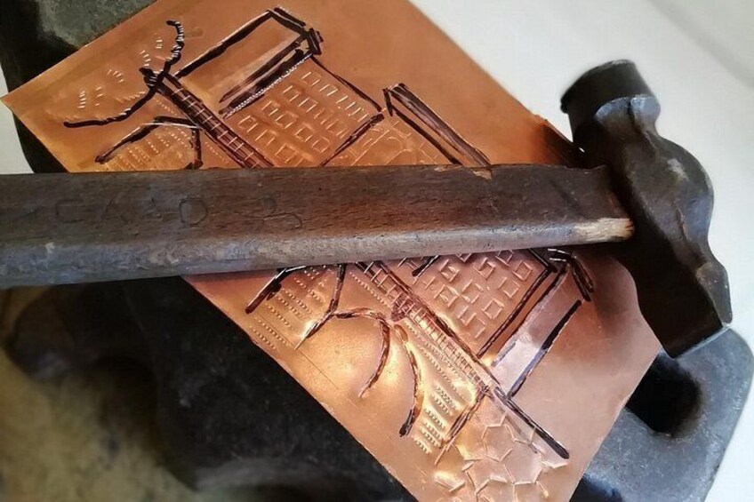 A hammer striking a copper sheet with embossed designs. 1