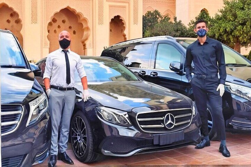 Two men standing beside a black Mercedes-Benz car in front of a building with arches. 4