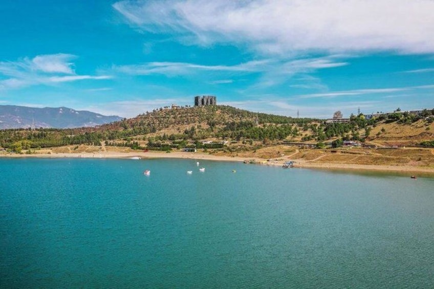 Paisaje costero con una colina, una masa de agua y un edificio lejano. 3