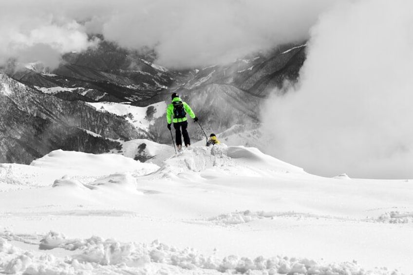 Una persona con un giubbotto verde acceso in piedi su una montagna innevata, con un bambino nelle vicinanze. 3