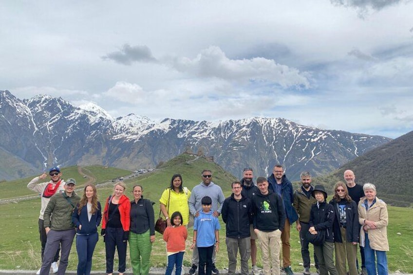 Un groupe de personnes se tient sur un champ herbeux, avec des montagnes enneigées en arrière-plan. 2