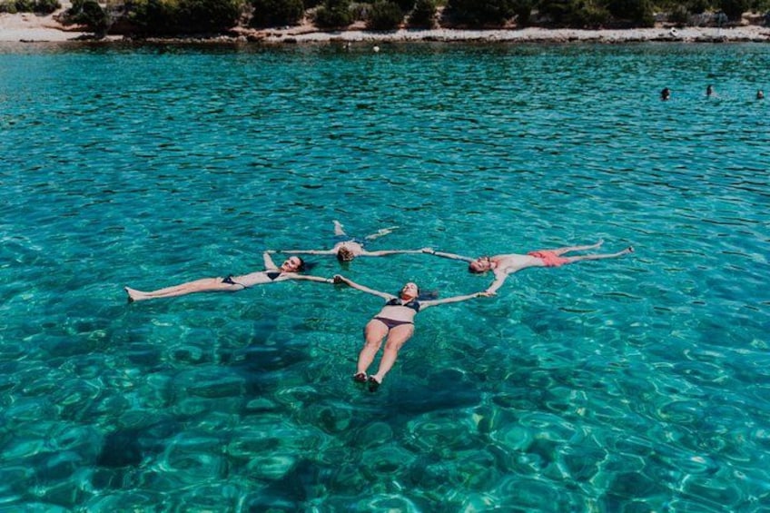 People floating on a clear turquoise sea with a beach in the background. 4