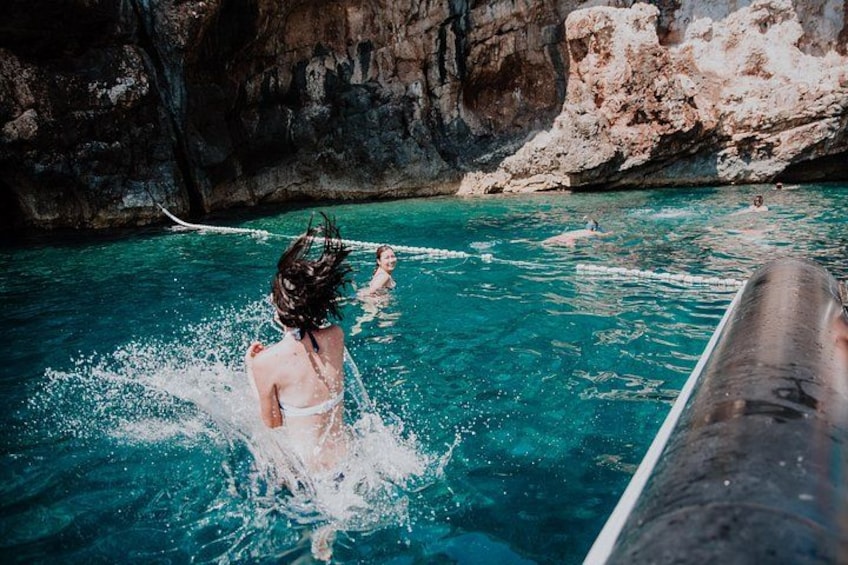 A person in a swimsuit splashing in clear blue water with rocky cliffs in the background. 3