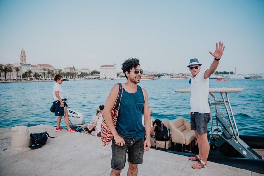 A waterfront scene with people near a boat, a cityscape in the background, and a clear sky. 2